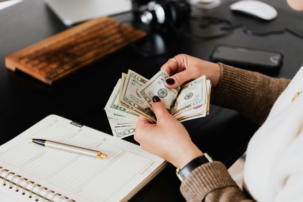 pexels-photo-4475524-4475524 Unrecognizable elegant female in sweater counting dollar bills while sitting at wooden table with planner and pen