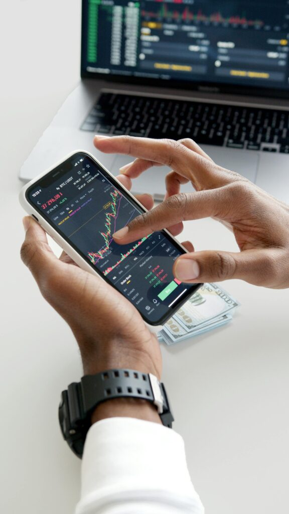 pexels-photo-6802049-6802049 Hands using smartphone trading app with charts, dollar bills in background.